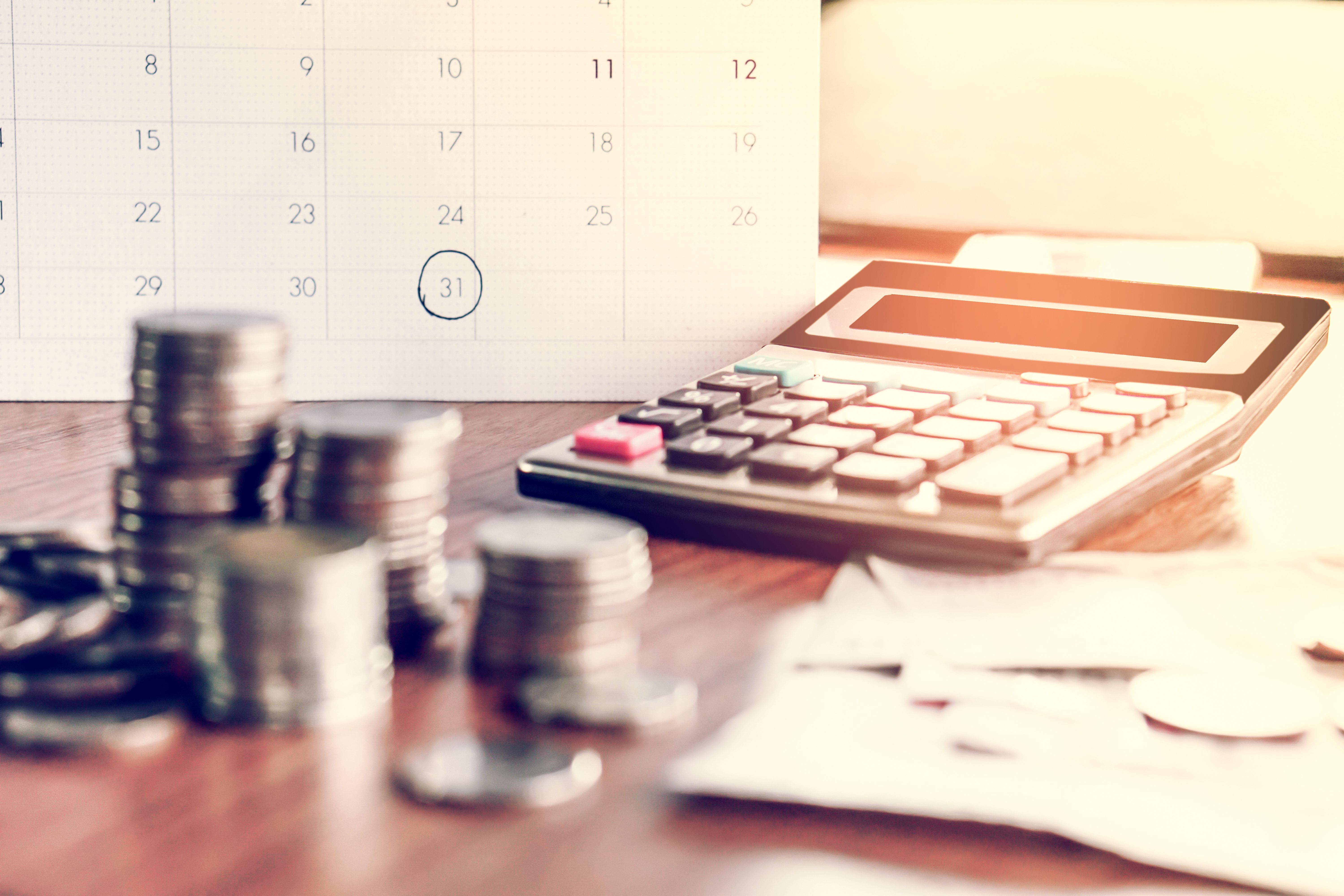 Calculadora, calendario y algunas monedas sobre un escritorio